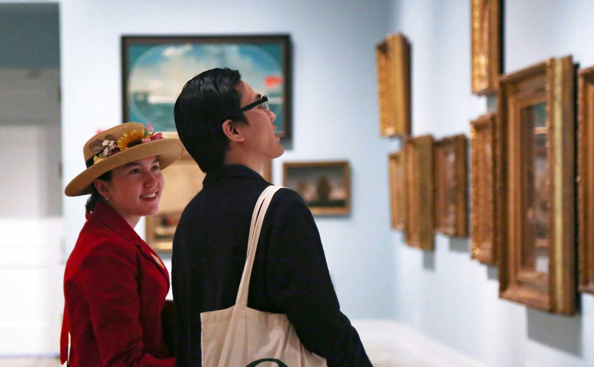 two museum visitors looking a gallery wall of framed artwork